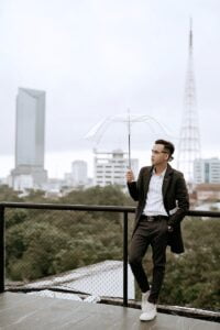 Stylish ethnic man with umbrella against modern city buildings