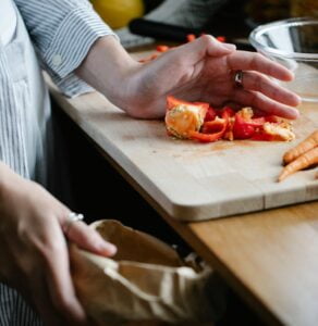 Crop anonymous housewife throwing vegetable leftovers on chopping board while cooking in light kitchen